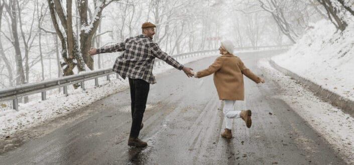 man and woman holding hands in the middle of a snowy street