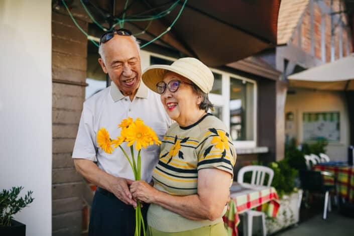 an old couple holding each other while the woman is holding flowers