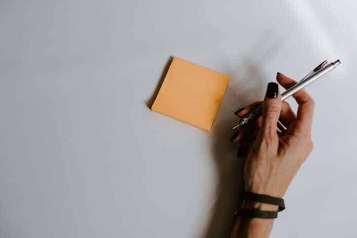 A hand holding a pen near a sticky note.