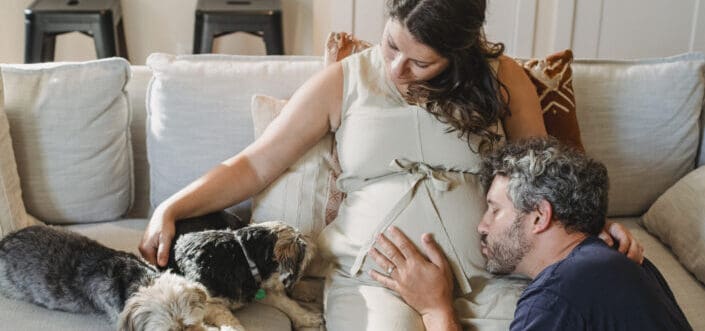 Happy pregnant couple with dogs on couch