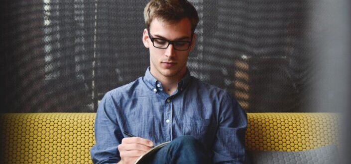 Man writing on his notebook while sitting on a sofa.