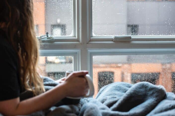 Woman having a coffee by the window while raining outside.