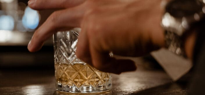 A person grabbing a glass of whiskey