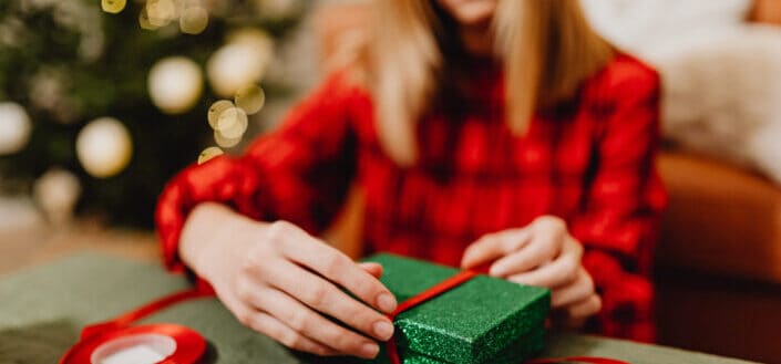 Girl in a red dress wrapping a green box with a red ribbon