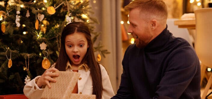 Surprised girl opening gift box near smiling father in house