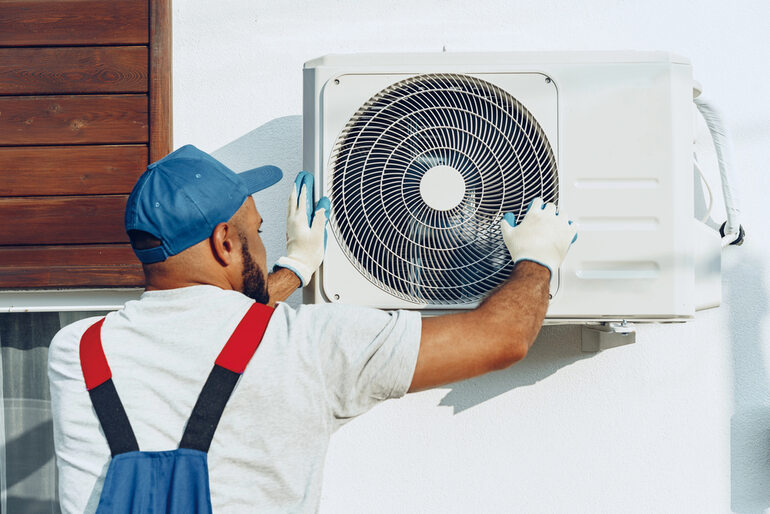 HVAC technician servicing an outdoor air conditioning unit, illustrating summer HVAC preparation for NYC apartment buildings. 