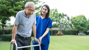 Older man using a walker with the support of a home caregiver, promoting safe mobility and independent living at home.