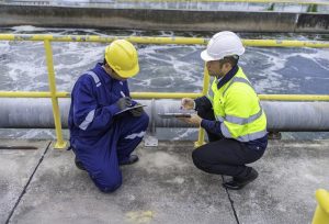 Two engineers in safety helmets inspecting wastewater flow at a treatment facility.
