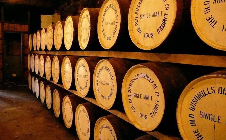 Rows of wooden whisky barrels stacked on racks inside a traditional distillery warehouse.